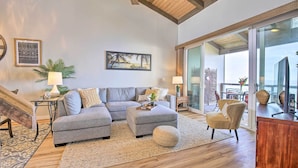 A modern living room with a sectional sofa, ottoman, and a large window overlooking a balcony. - Airy Oceanfront Kailua-kona Gem w/ Community Pool (Kailua-Kona)
