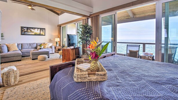 A spacious living area with a large bed, a sofa, and a television. There is a view of the ocean through large windows. - Airy Oceanfront Kailua-kona Gem w/ Community Pool (Kailua-Kona)