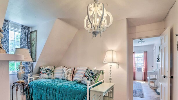 A bedroom with a sloped ceiling, a bed with a teal bedspread, a chandelier, a bedside table, and a lamp. - Charming Nineteenth-century Cape Code Escape (Centerville)