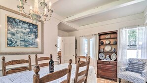 A dining area with a wooden table and chairs, a chandelier, a painting, and a shelf with decorative plates. - Charming Nineteenth-century Cape Code Escape (Centerville)