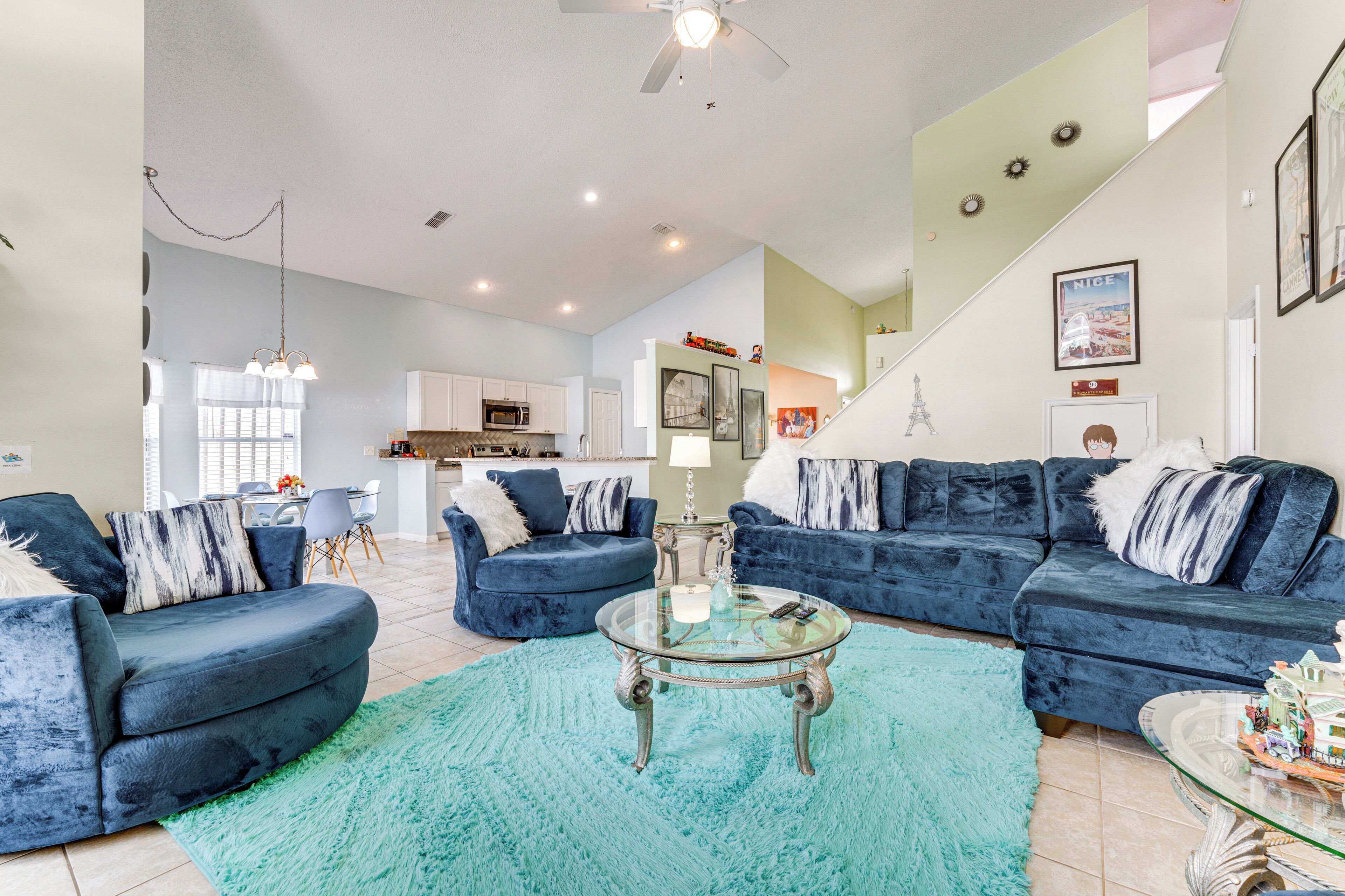 A spacious living room with two blue sofas, a glass coffee table, and a teal rug.