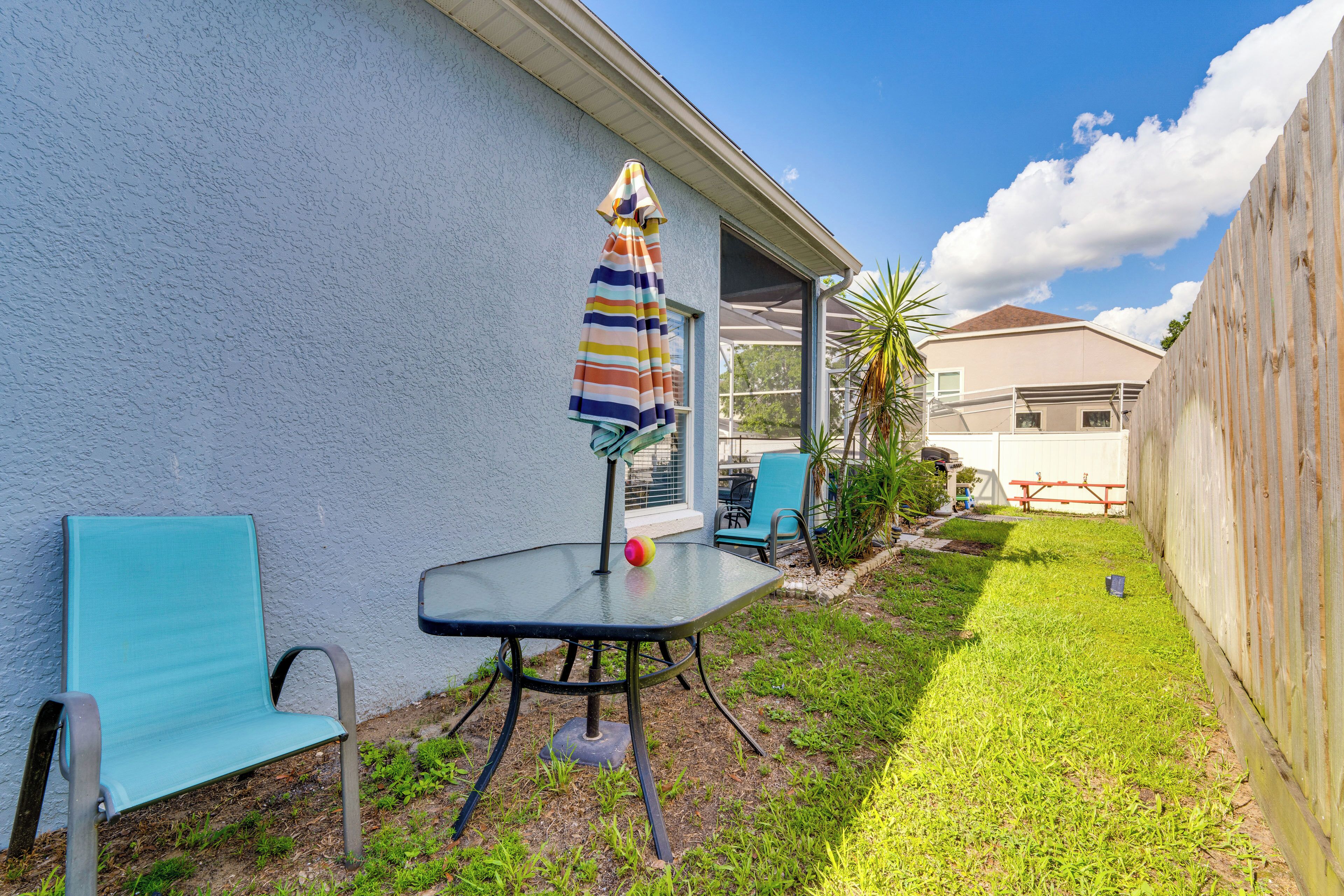 A patio with a table and chairs, a striped umbrella, and a view of a house in the background.