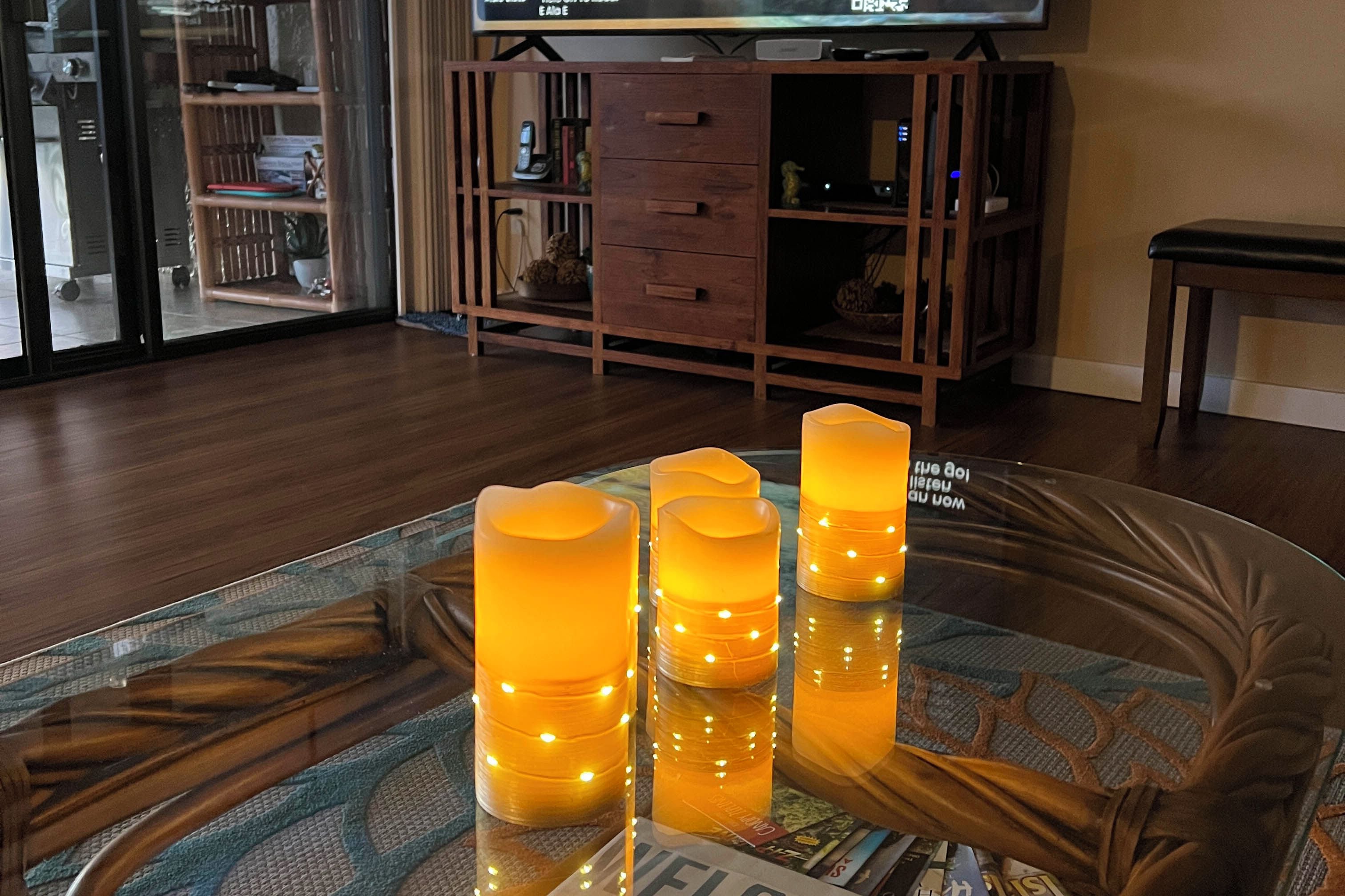 Lasinen pöytä, jonka päällä on neljä kynttilää, puinen kaappi ja taustalla televisio.