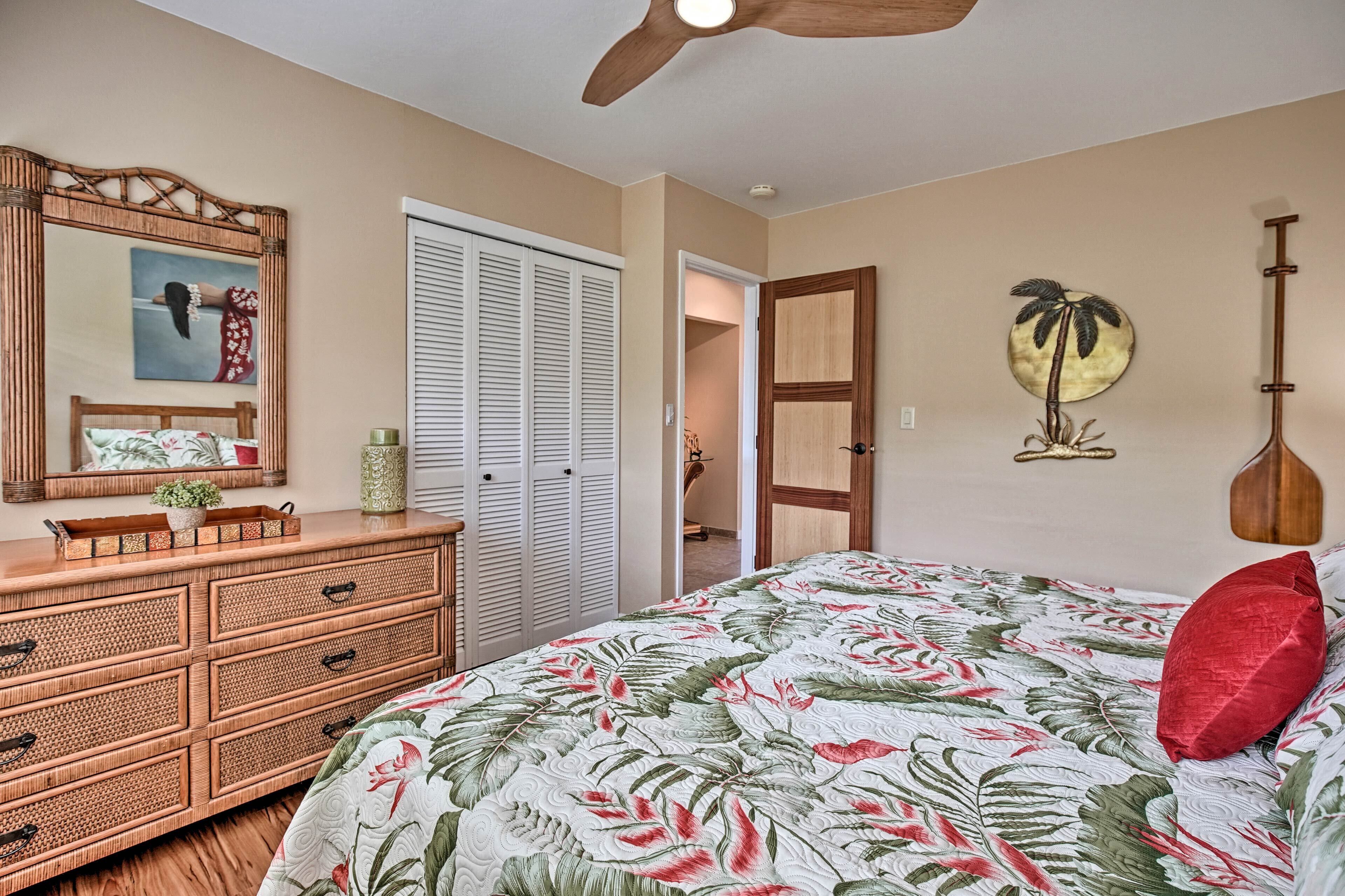 A bedroom with a bed, a dresser, a ceiling fan, a door, and a wall with a decorative piece.