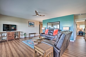 A living room with a leather sofa, a television, a ceiling fan, and a wooden floor. - Ocean-view Lanai! Resort Condo on Kona Coast (Kailua-Kona)