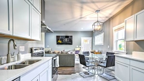 A modern kitchen with white cabinets, a stainless steel sink, and a dining area with a glass table and black chairs. - Pet-friendly Minneapolis Home ~ 6 Mi to Dtwn! (Minneapolis)