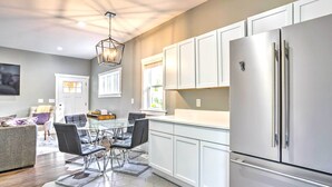 A modern kitchen with white cabinets, a stainless steel refrigerator, and a glass dining table with black chairs. - Pet-friendly Minneapolis Home ~ 6 Mi to Dtwn! (Minneapolis)