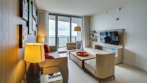Un salon moderne doté d’un grand téléviseur, de sièges confortables, d’une table basse et offrant une vue sur la mer grâce à de grandes fenêtres.