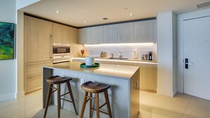 Une cuisine moderne dotée d’un îlot central, de deux tabourets de bar, de meubles de rangement en bois et d’un four encastré.