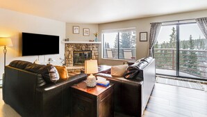 A living room with a stone fireplace, leather sofas, a flat-screen TV, and a large window with a view of trees. - 11 Mi to Keystone Resort: Condo in Silverthorne (Silverthorne)