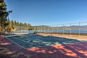 Un court de tennis en plein air, doté d’un filet et entouré d’une clôture, avec une étendue d’eau en arrière-plan.