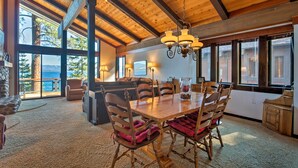 A spacious dining area with a wooden table and chairs, large windows offering a view of the outdoors, and a high ceiling with exposed beams. - 11 Mi to Palisades Tahoe: Lakefront Home w/ View! (Tahoe City)