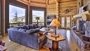 Interior acogedor de una cabaña de troncos con un sofá de cuero, chimenea de piedra y grandes ventanales con vistas al exterior.