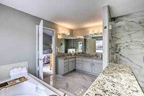 A modern bathroom with a large mirror, granite countertops, and a marble floor.