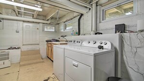 Une buanderie équipée de plusieurs sèche-linge superposés, d’une machine à laver et d’une fenêtre.