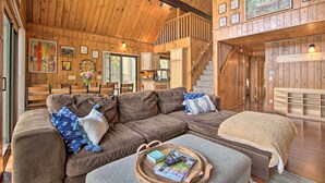L’intérieur chaleureux d’un chalet avec un grand canapé d’angle marron, une table à manger en bois et un escalier menant à un niveau supérieur.