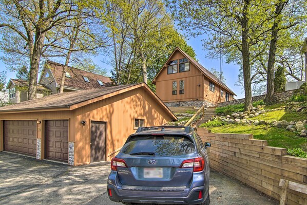 A Subaru Outback parked in a driveway with a wooden garage and a house in the background.