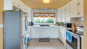 A kitchen with white cabinets, stainless steel appliances, a window with a view, and a patterned ceiling light. - Waterfront Algoma Vacation Rental on Lake Michigan (Algoma)