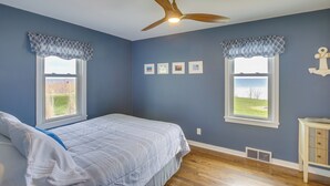 A bedroom with a bed, two windows with patterned valances, a ceiling fan, and a small cabinet. - Waterfront Algoma Vacation Rental on Lake Michigan (Algoma)