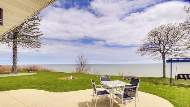 A patio with a table and chairs, a bench, and a view of a lake. - Waterfront Algoma Vacation Rental on Lake Michigan (Algoma)
