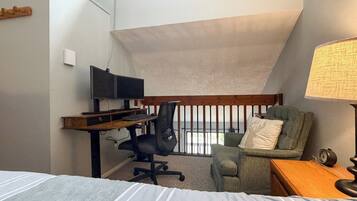 Ein Schlafzimmer mit Bett, Schreibtisch, Computer, Stuhl, Lampe und Blick ins Freie.