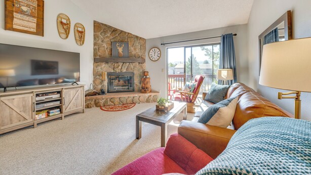 A cozy living room with a stone fireplace, a television, a leather sofa, and a large window with curtains. - Warm Fraser Townhome w/ Community Amenities! (Fraser)