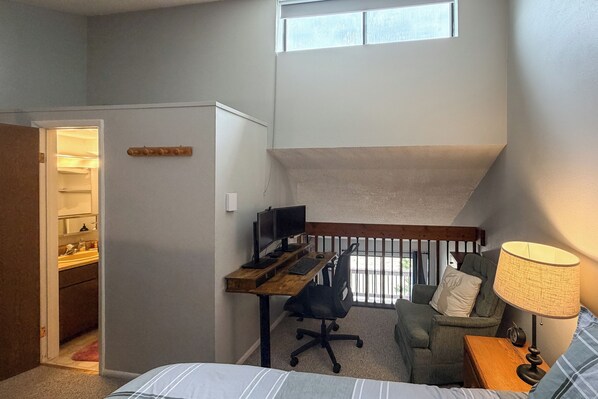 Un dormitorio con cama, escritorio con computadora, silla, lámpara y ventana.