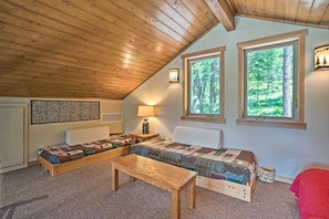 Un dormitorio acogedor con cama rústica tipo altillo, un banco de madera y vistas al bosque a través de amplios ventanales.