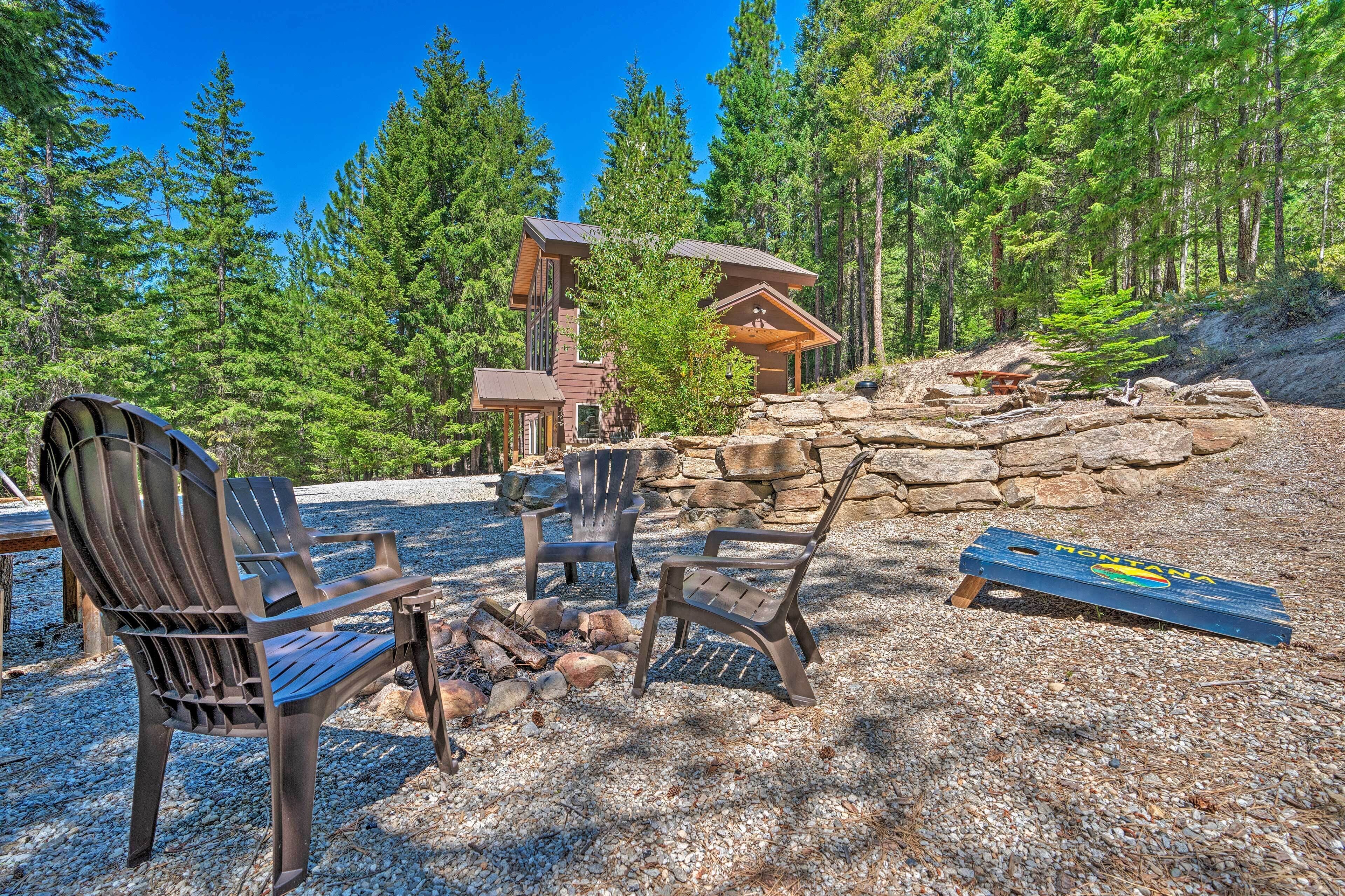 A lodge with a stone fireplace, Adirondack chairs, and a deck overlooking a forest.