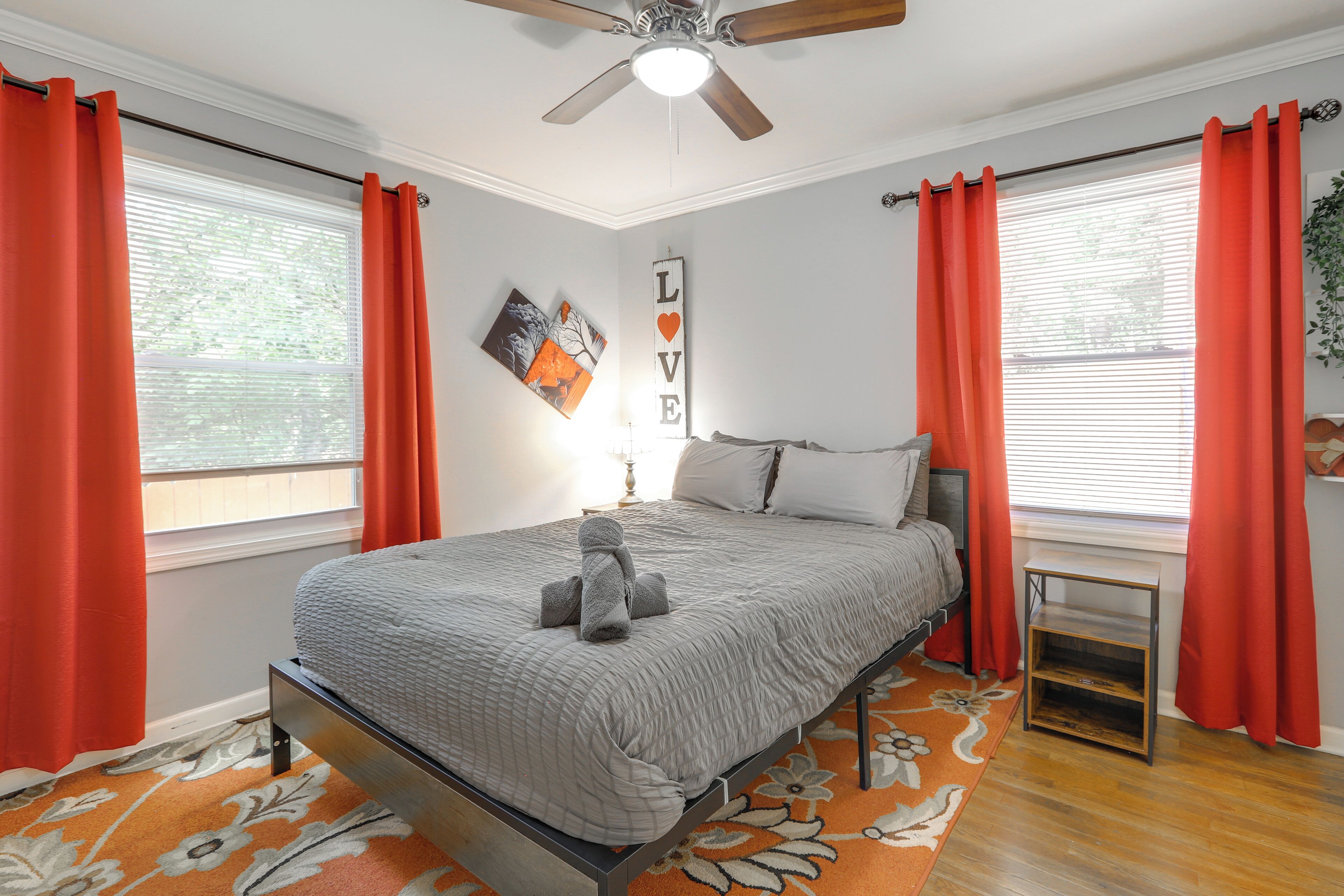 A bedroom with a bed, a ceiling fan, a wall-mounted shelf, and a window with curtains.