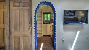 A hallway with a wooden door, a blue decorative archway, and a kitchen area with cabinets and a window. - Charming Casita Studio - Near Santa Fe Plaza! (Santa Fe)