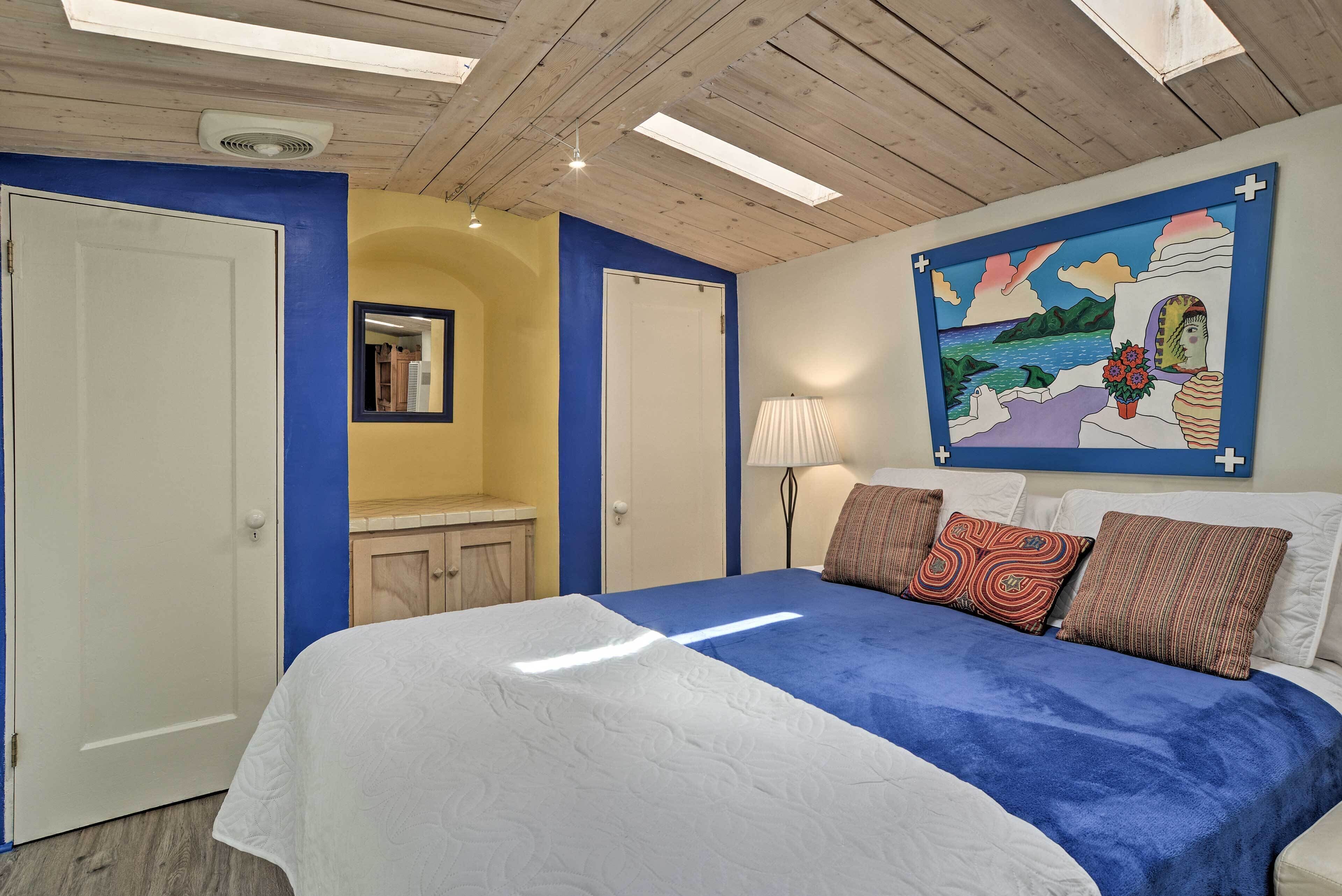 A bedroom with a bed, a painting, and a ceiling fan.