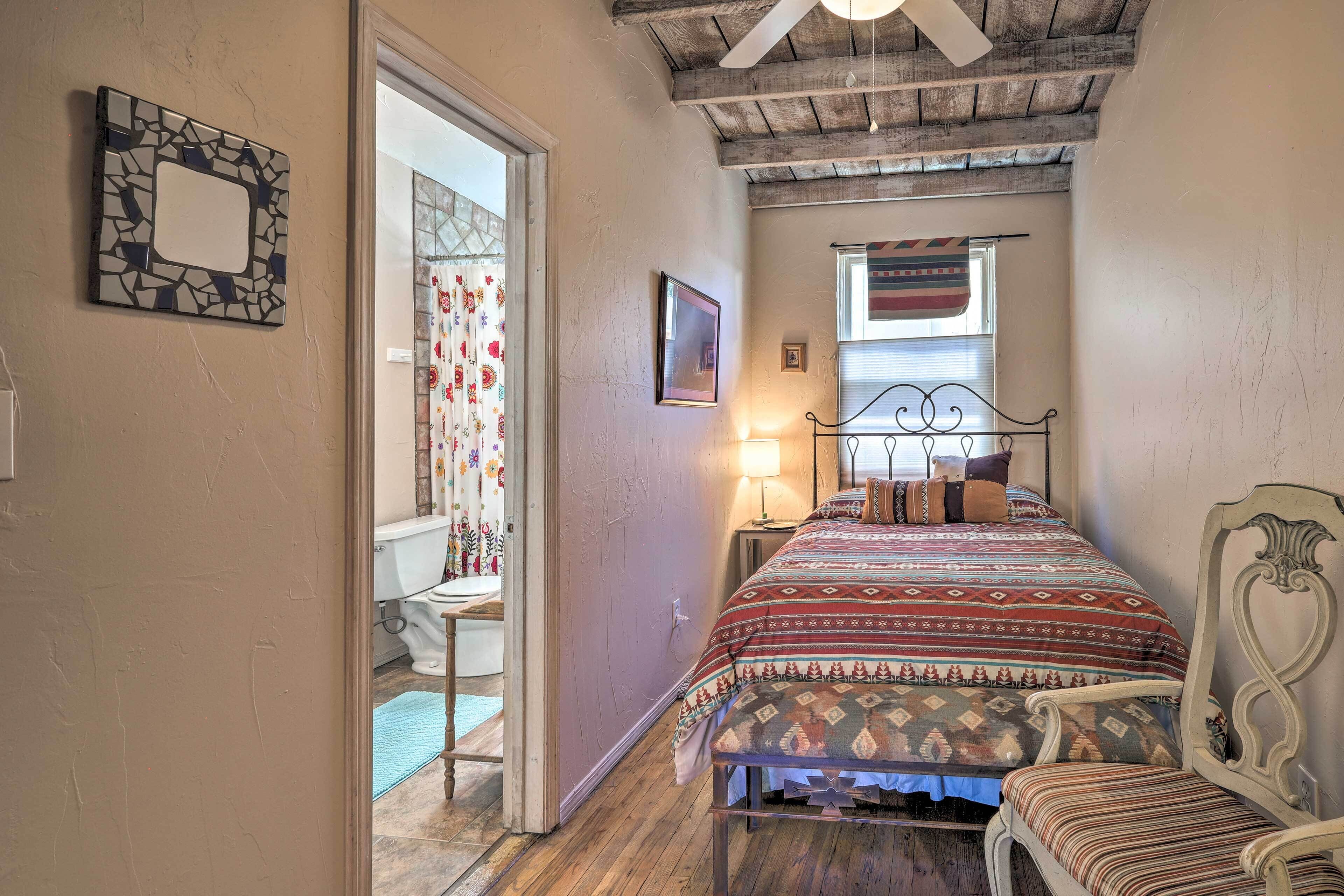 A bedroom with a bed, a chair, a bedside table, a window with curtains, and a ceiling fan.