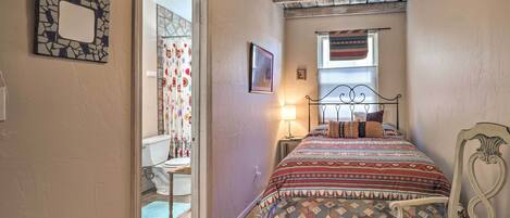 A bedroom with a bed, a chair, a bedside table, a window with curtains, and a ceiling fan.