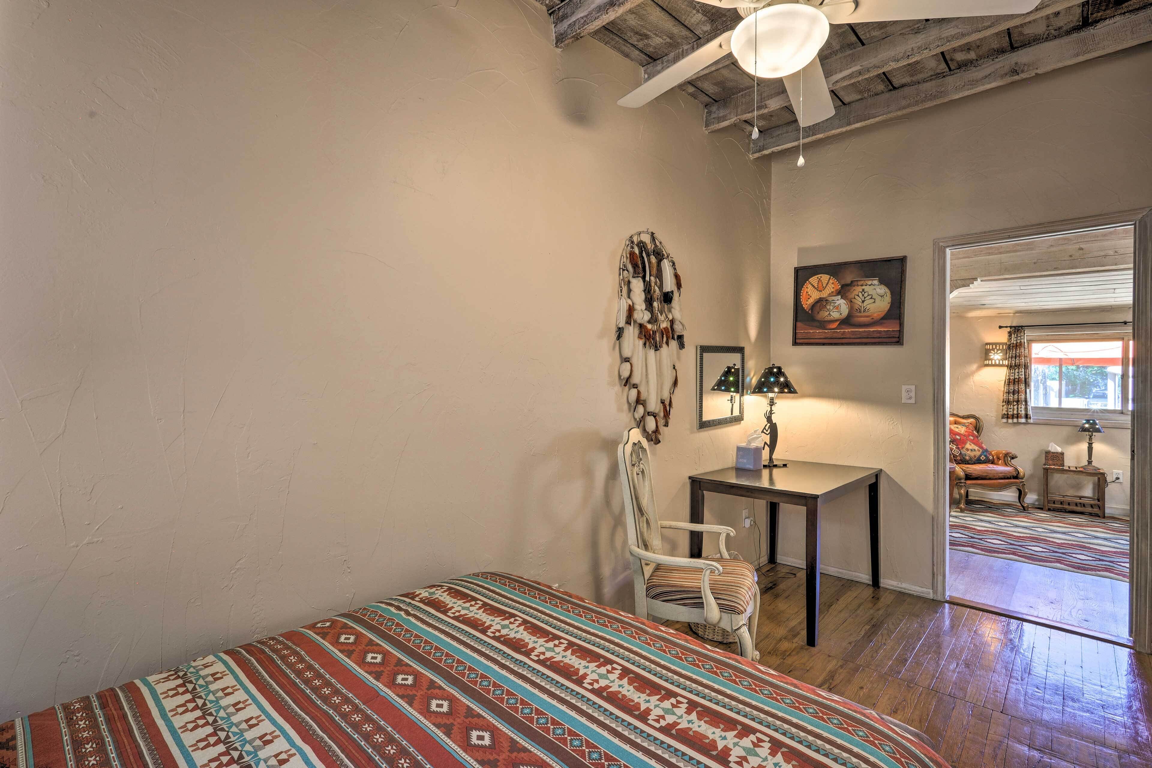 A room with a bed, a chair, a table, and a painting on the wall.