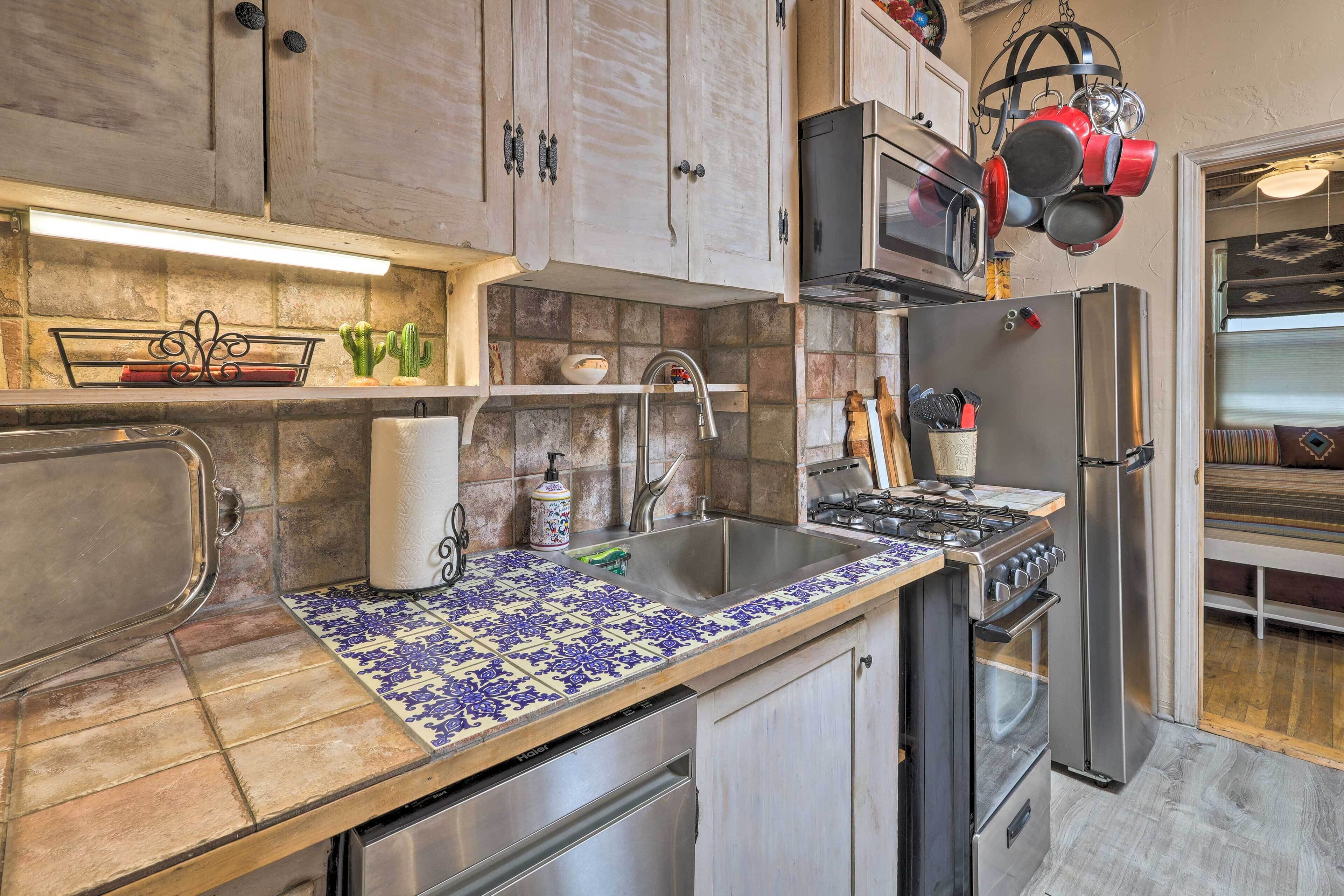 Una cocina con salpicadero de azulejos, electrodomésticos de acero inoxidable y una barra para colgar ollas.