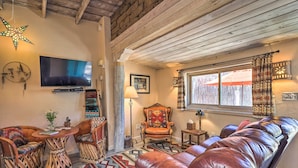 Un salon chaleureux avec un plafond en bois, un grand téléviseur à écran plat, un tapis à motifs, un canapé en cuir et un luminaire en forme d’étoile.