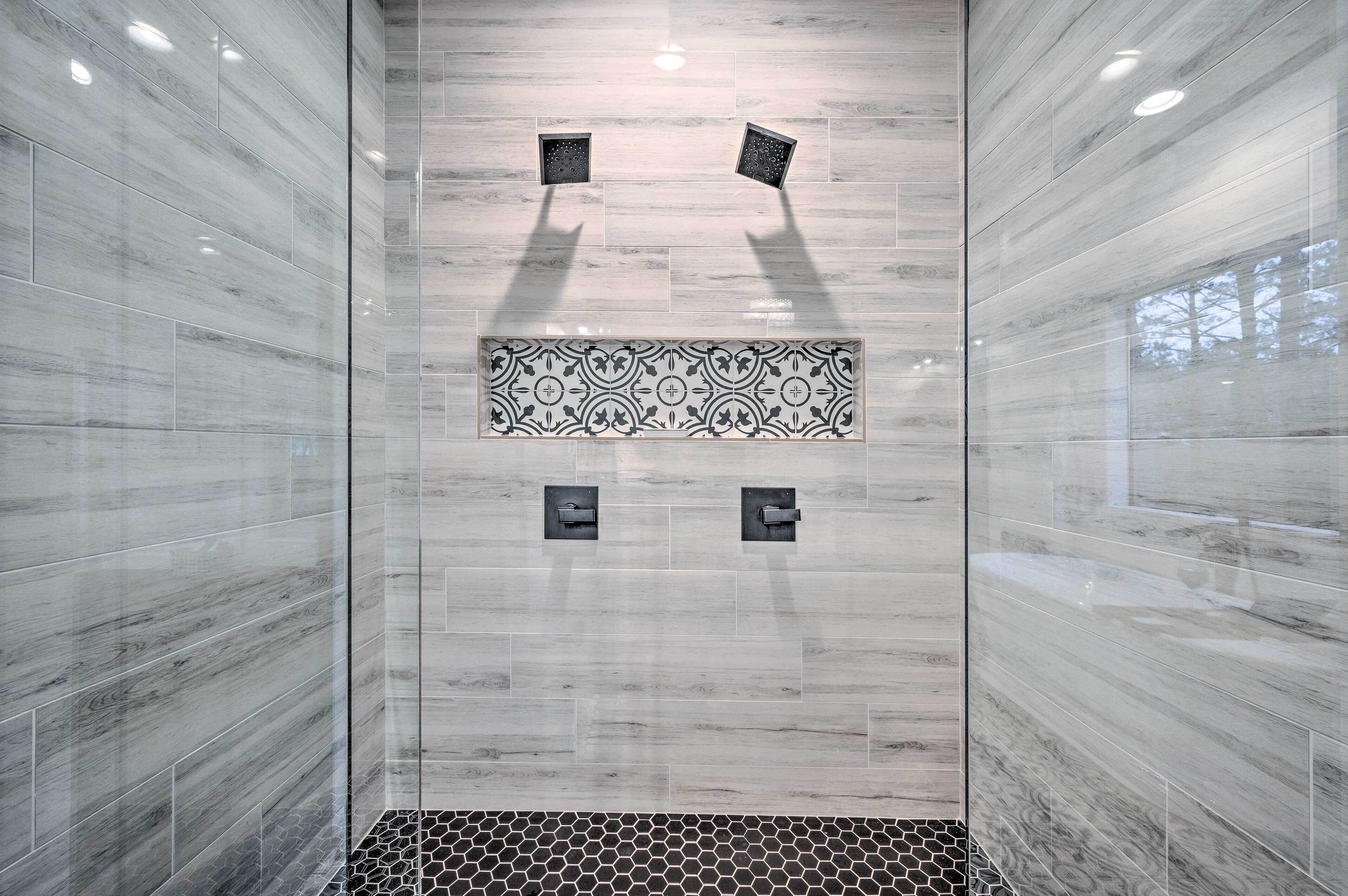 A modern bathroom with a large mirror, a patterned tile accent, and a black and white mosaic floor.