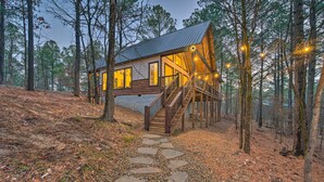 A cabin with a wooden staircase leading to a deck, surrounded by trees. - Modern Cabin w/ Hot Tub: 1 Mi From Hochatown! (Broken Bow)