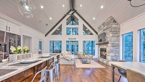 A spacious kitchen with a large island, a stone fireplace, and a view of the outdoors. - Modern Cabin w/ Hot Tub: 1 Mi From Hochatown! (Broken Bow)