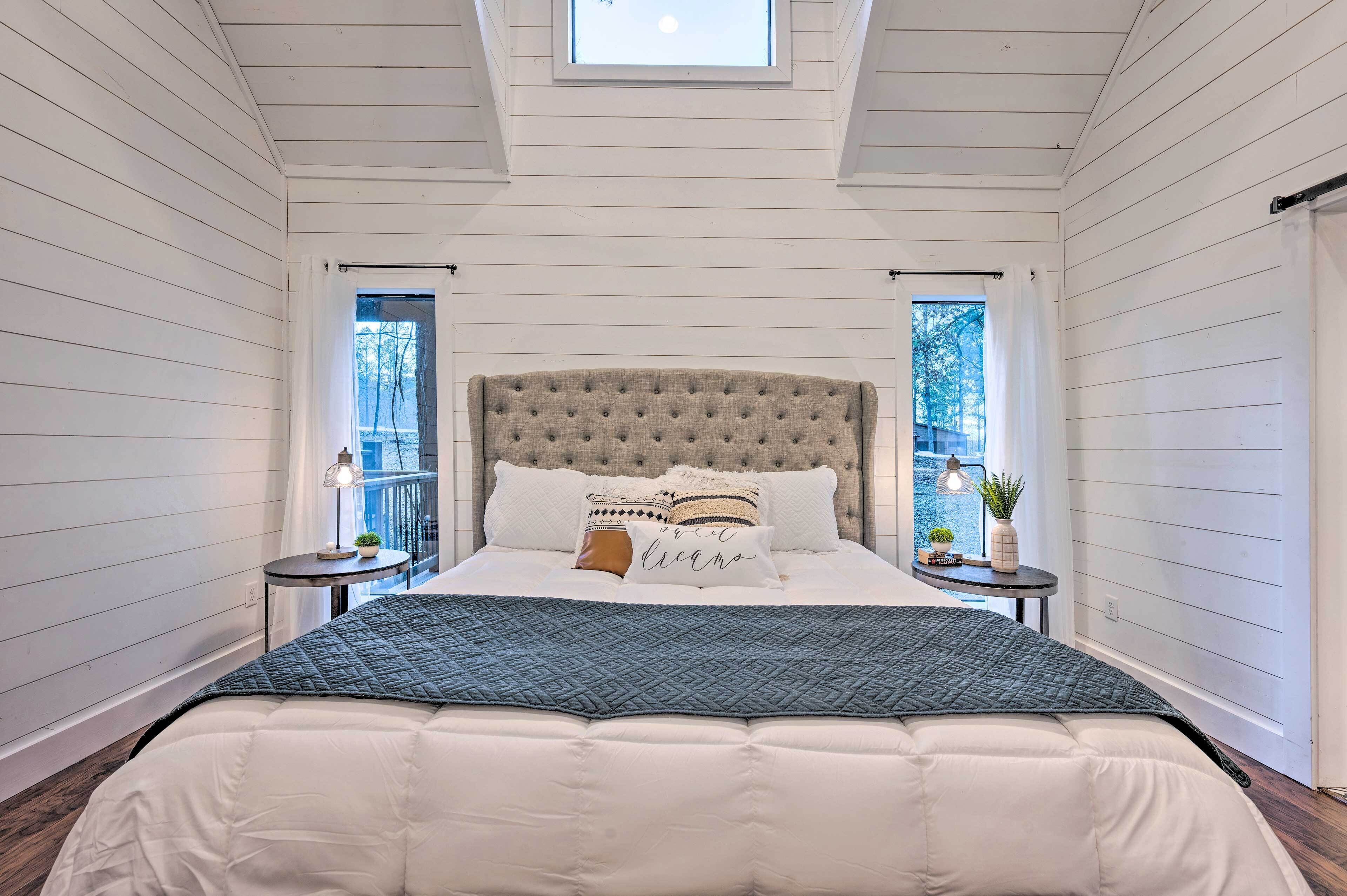 A bedroom with a large bed, a tufted headboard, two bedside tables with lamps, and a skylight above.