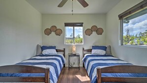 Quarto com duas camas, ventilador de teto, janela com vista para o verde e conchas decorativas na parede.