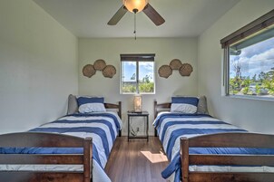 Un dormitorio con dos camas, un ventilador de techo, una ventana con vista a la vegetación y conchas decorativas en la pared.
