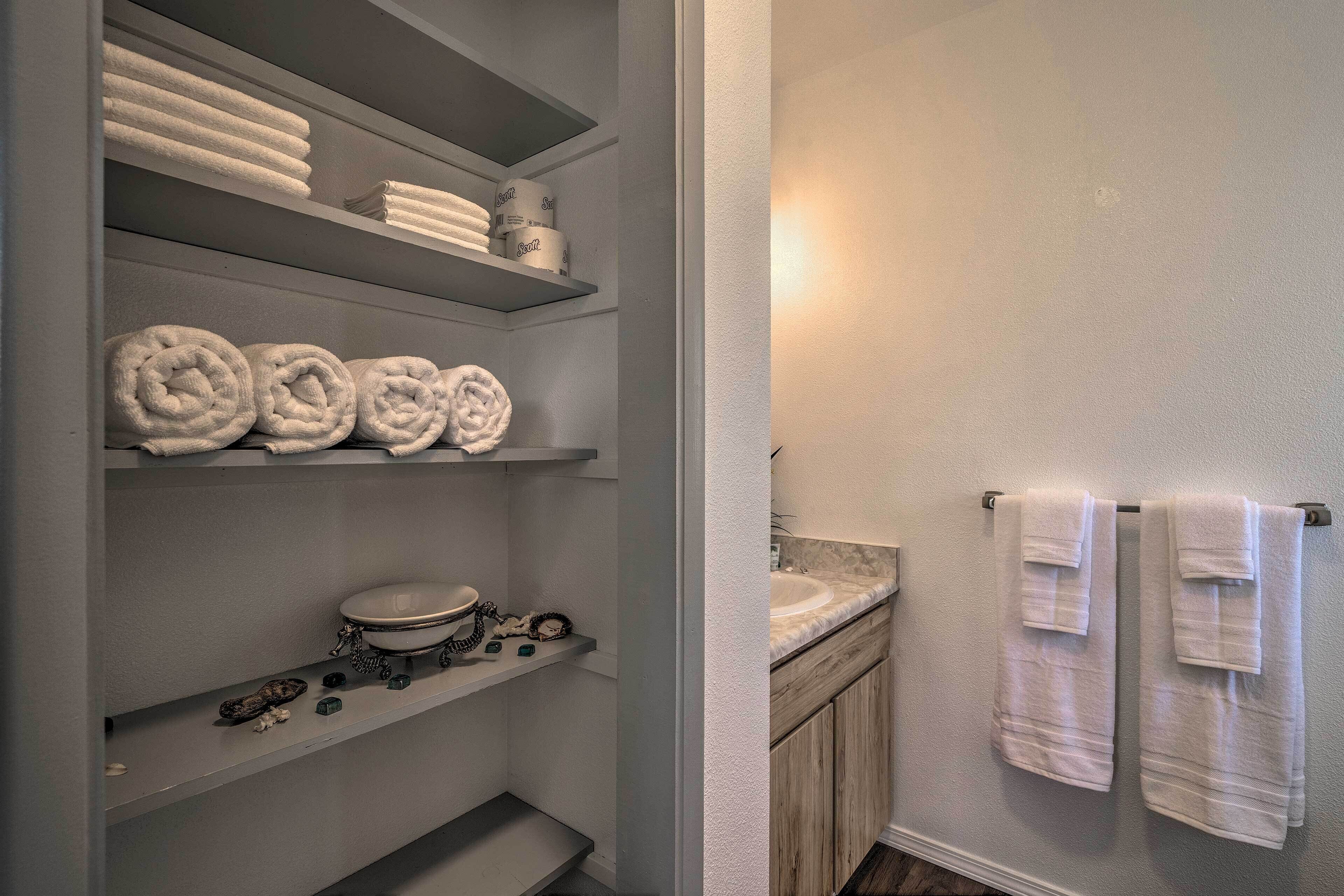 Een badkamer met toilet, wastafel en planken met handdoeken en toiletartikelen.