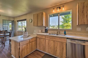 Una cocina con armarios de madera, lavavajillas de acero inoxidable y un ventanal con vistas a árboles.