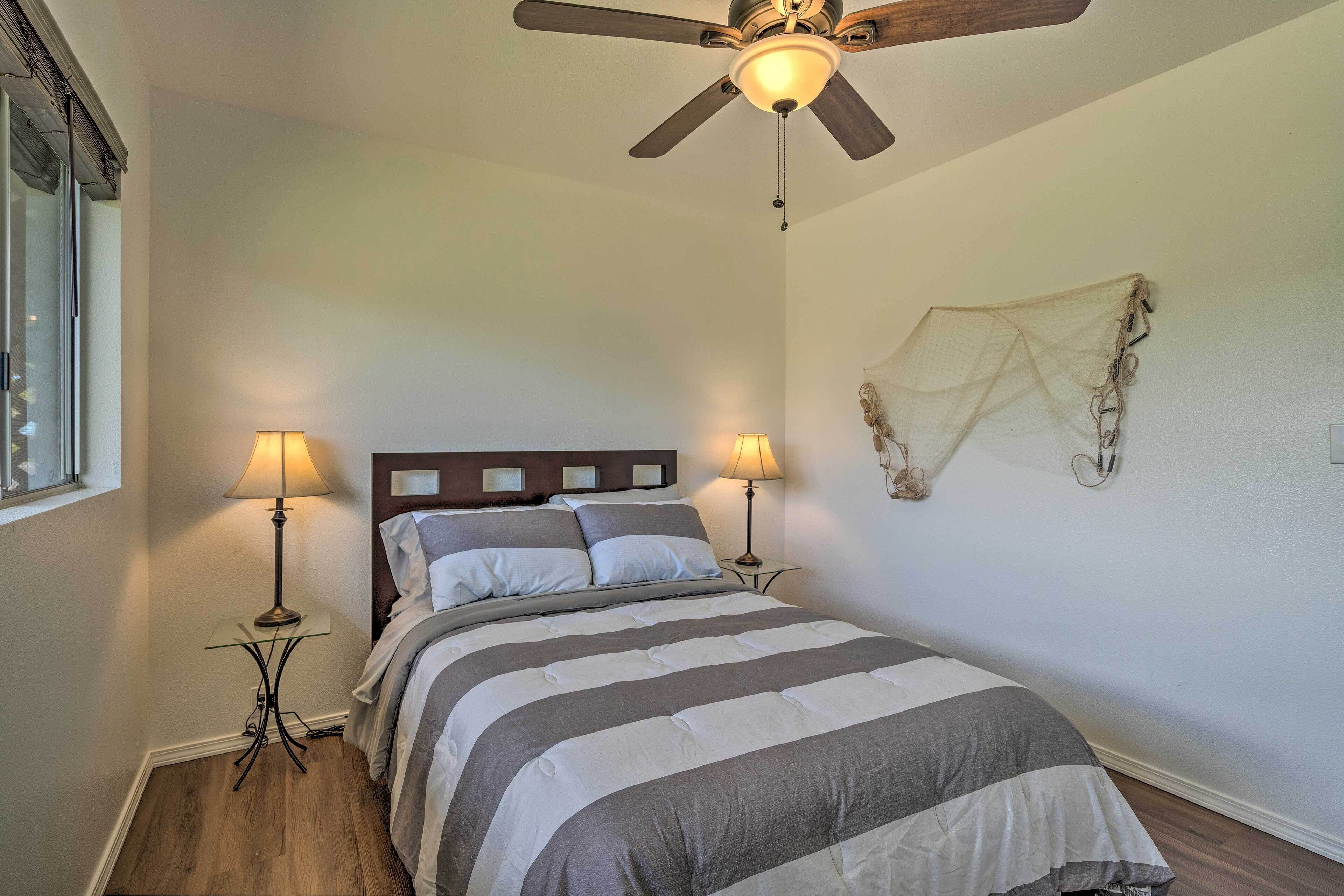 Une chambre à coucher comprenant un lit, deux lampes de chevet, un ventilateur de plafond et un élément décoratif mural.