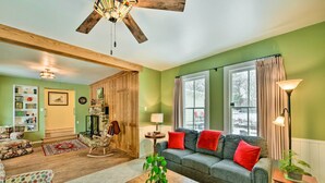 A cozy living room with a wooden ceiling, a green wall, a grey sofa with red cushions, a wooden coffee table, and a rocking chair. - Charming Buena Vista Creekside Home: Walk to Main! (Buena Vista)