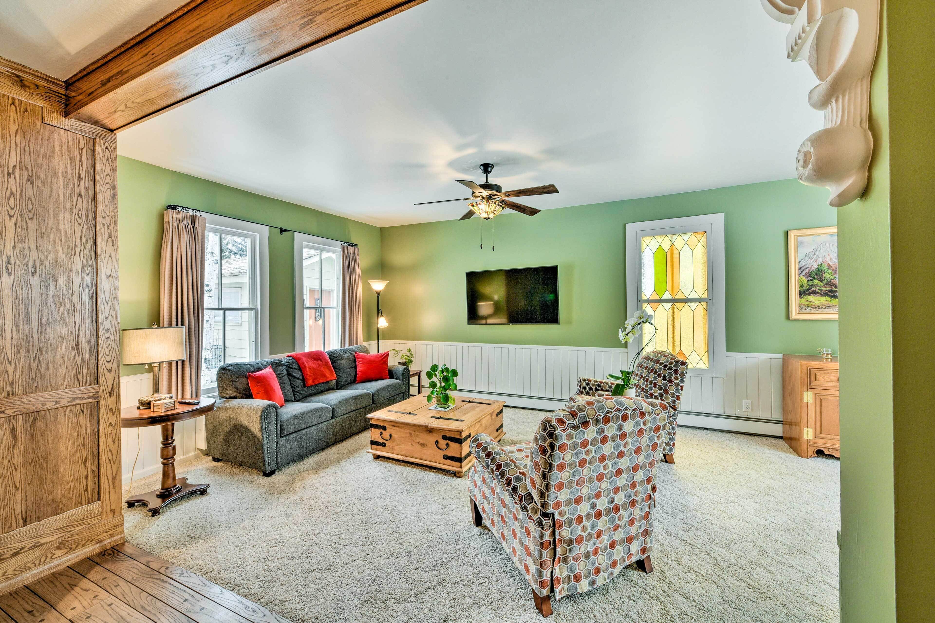 A living room with a wooden ceiling, a ceiling fan, a sofa, a patterned armchair, a wooden coffee table, and a lamp.