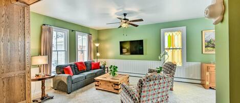 A living room with a wooden ceiling, a ceiling fan, a sofa, a patterned armchair, a wooden coffee table, and a lamp.