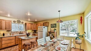 A modern kitchen with wooden cabinets, a central island, and a dining area set for a meal. - Charming Buena Vista Creekside Home: Walk to Main! (Buena Vista)